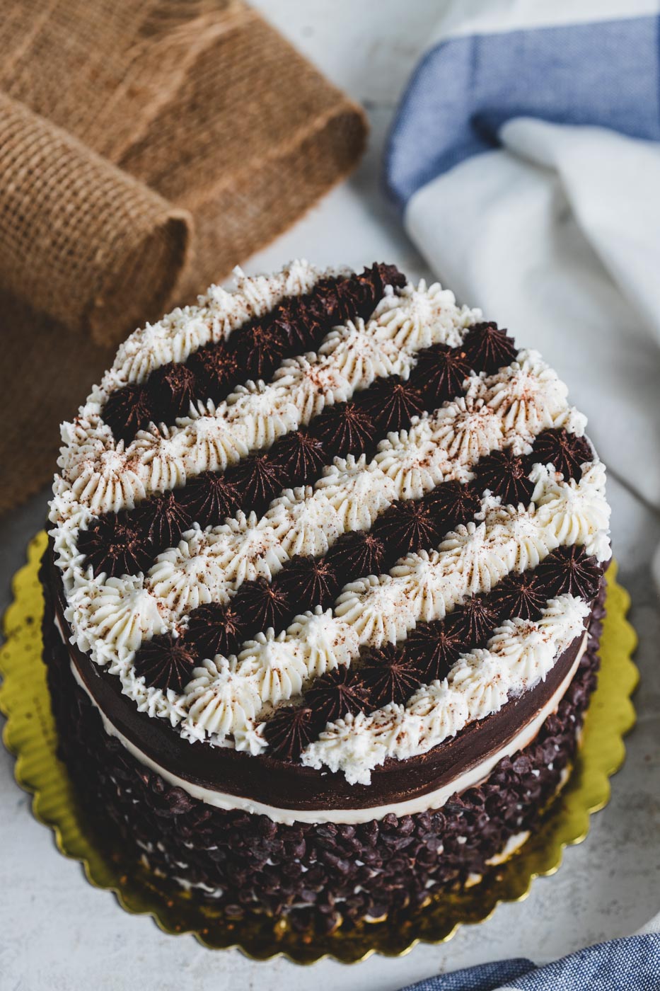A cake with elaborate chocolate and vanilla striped decorative icing rolled in chocolate chips and lightly dusted with cocoa powder
