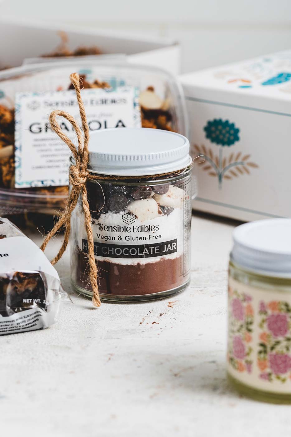 CLose up of a jar of hot chocolate mix with an open gift box and other treats in the background
