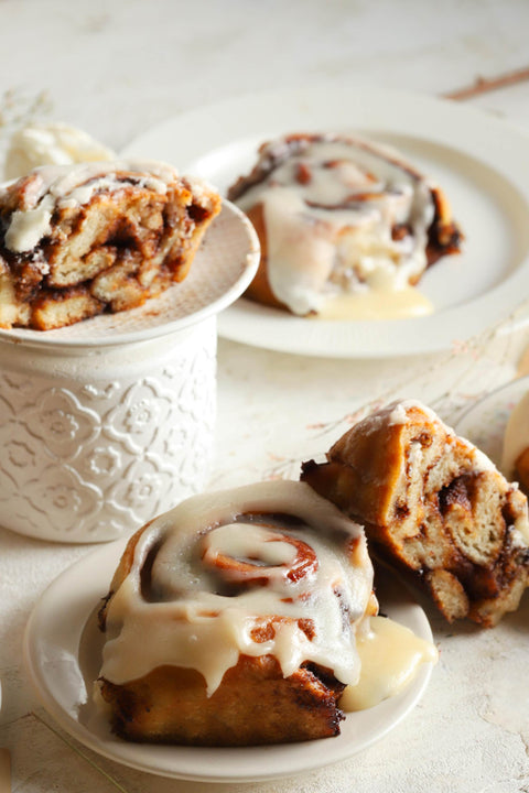 Cinnamon rolls with icing on white plates on a light background