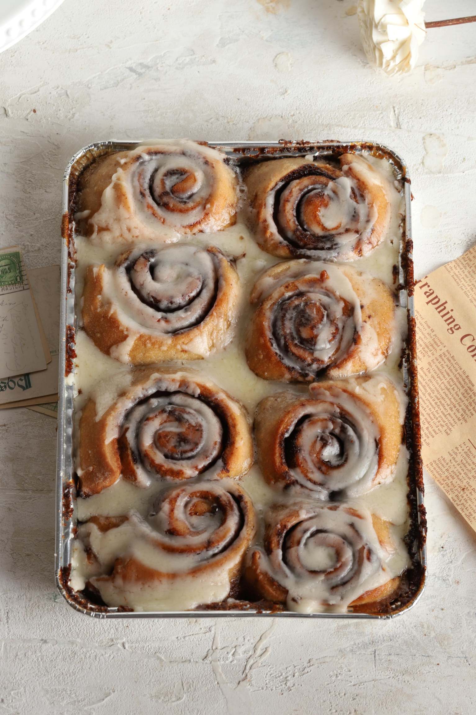 Baking tray with cinnamon rolls covered in white icing on a light background