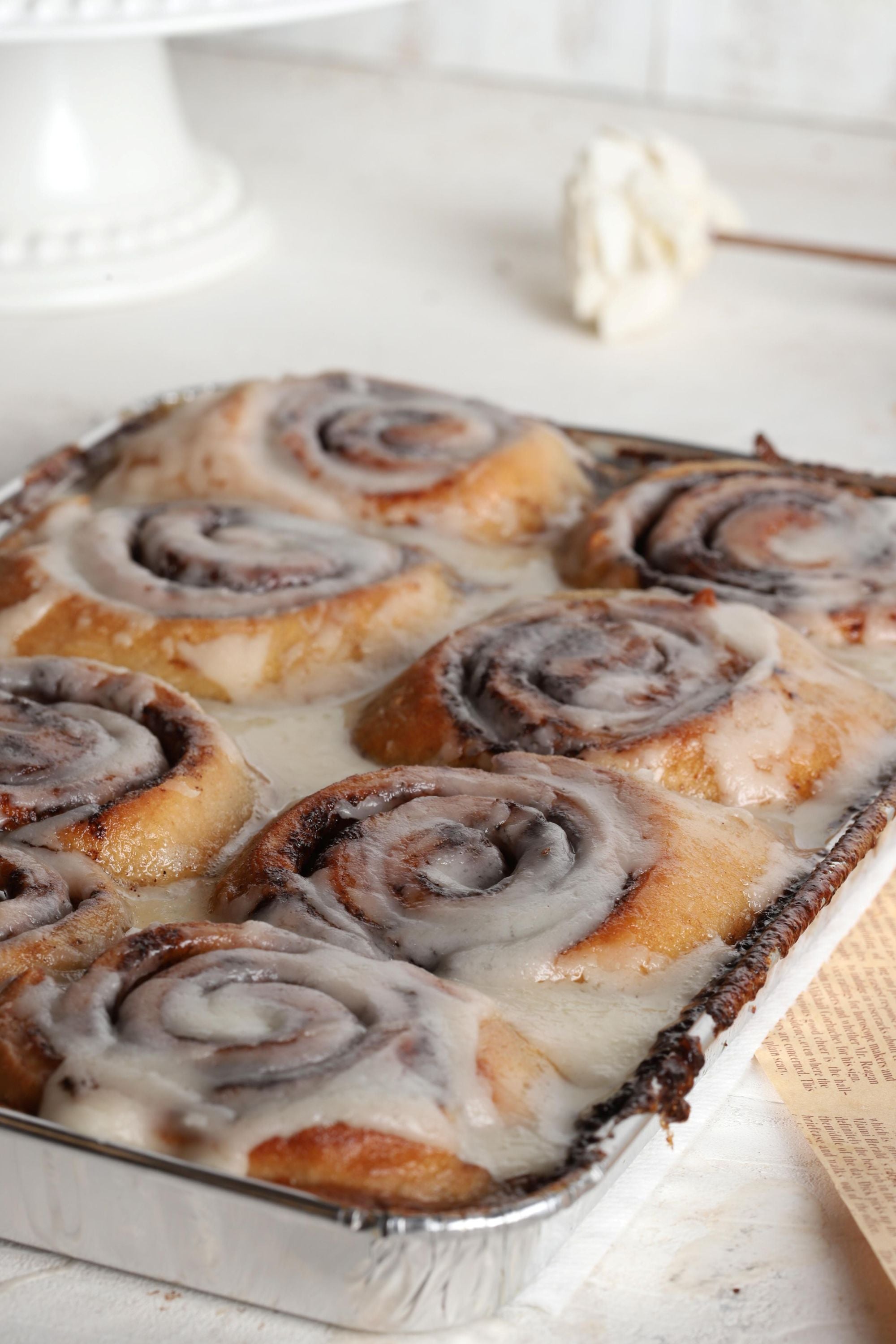 Baked cinnamon rolls with icing in a baking dish on a white surface.
