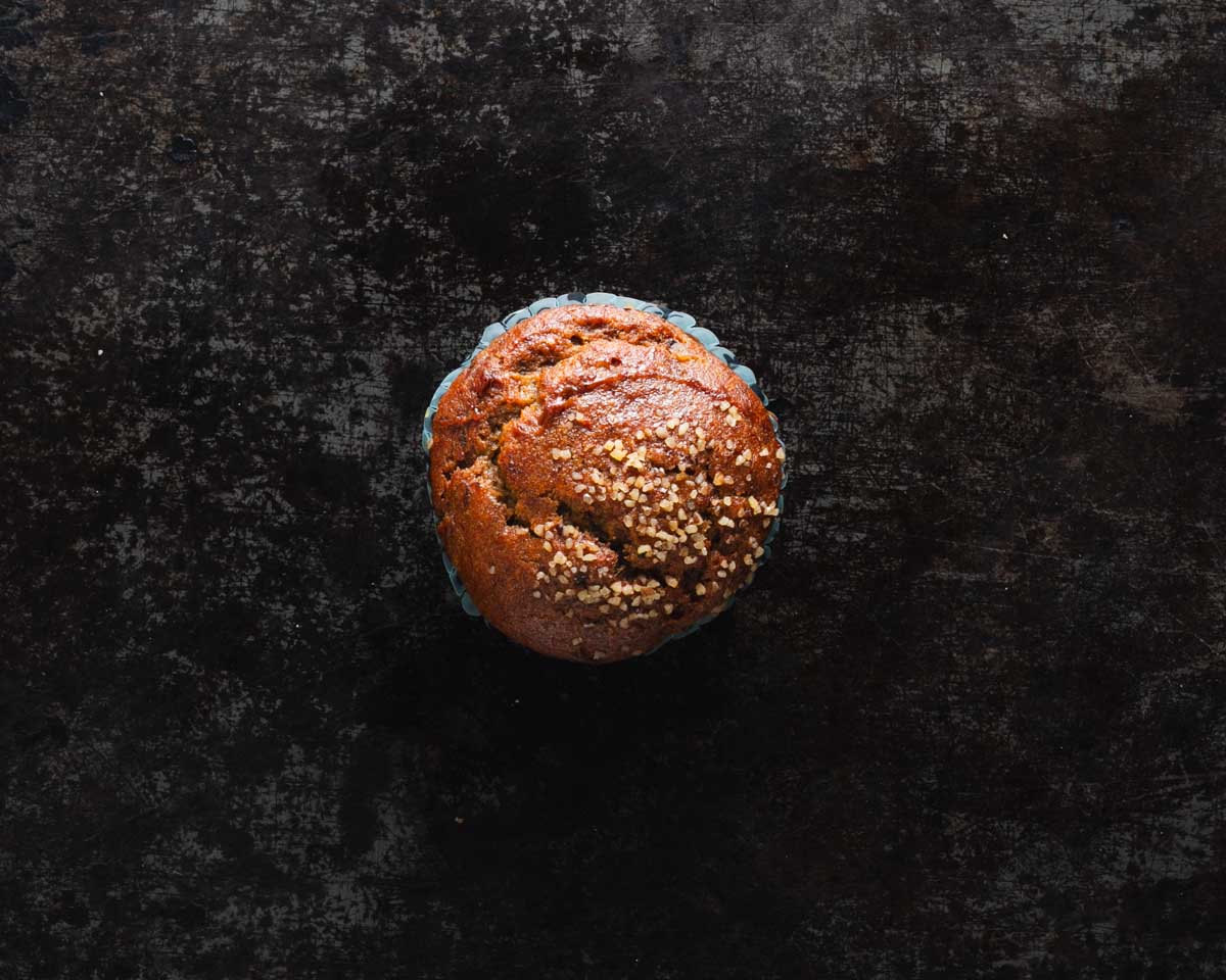 Top view of a banana walnut muffin topped with chopped walnuts on a dark textured surface.