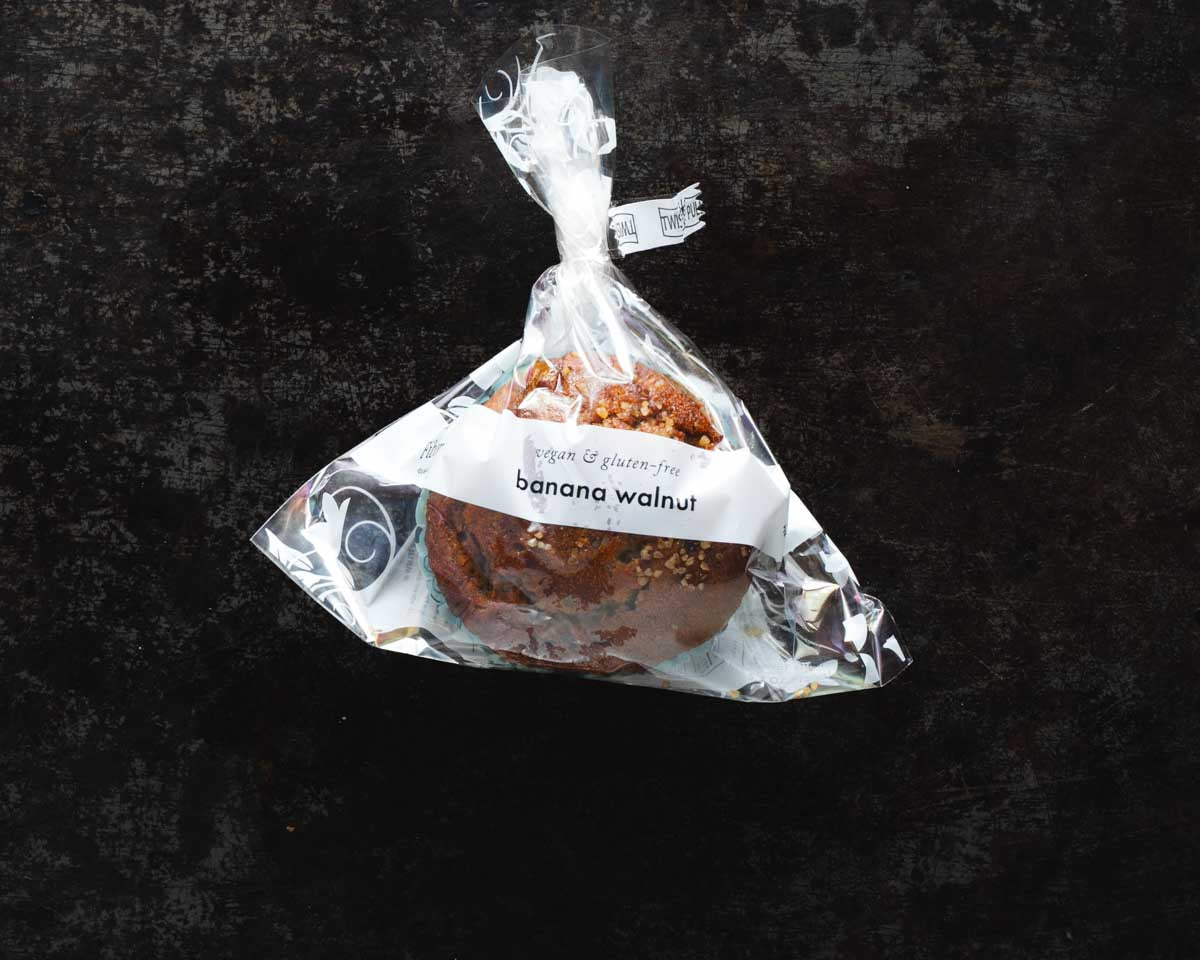 Packaged vegan and gluten-free banana walnut muffin in a clear packaging against a dark textured background.