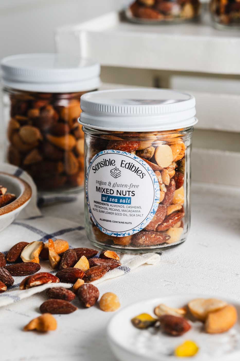 Jars of salted mixed nuts with more nuts piled around them