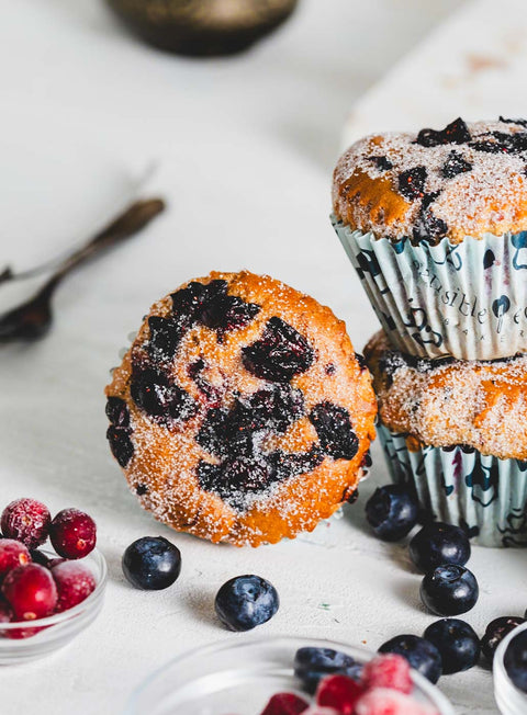 Vanilla berry muffin topped with powdered sugar and mixed berries, resting on its side with more muffins and berries in the background.