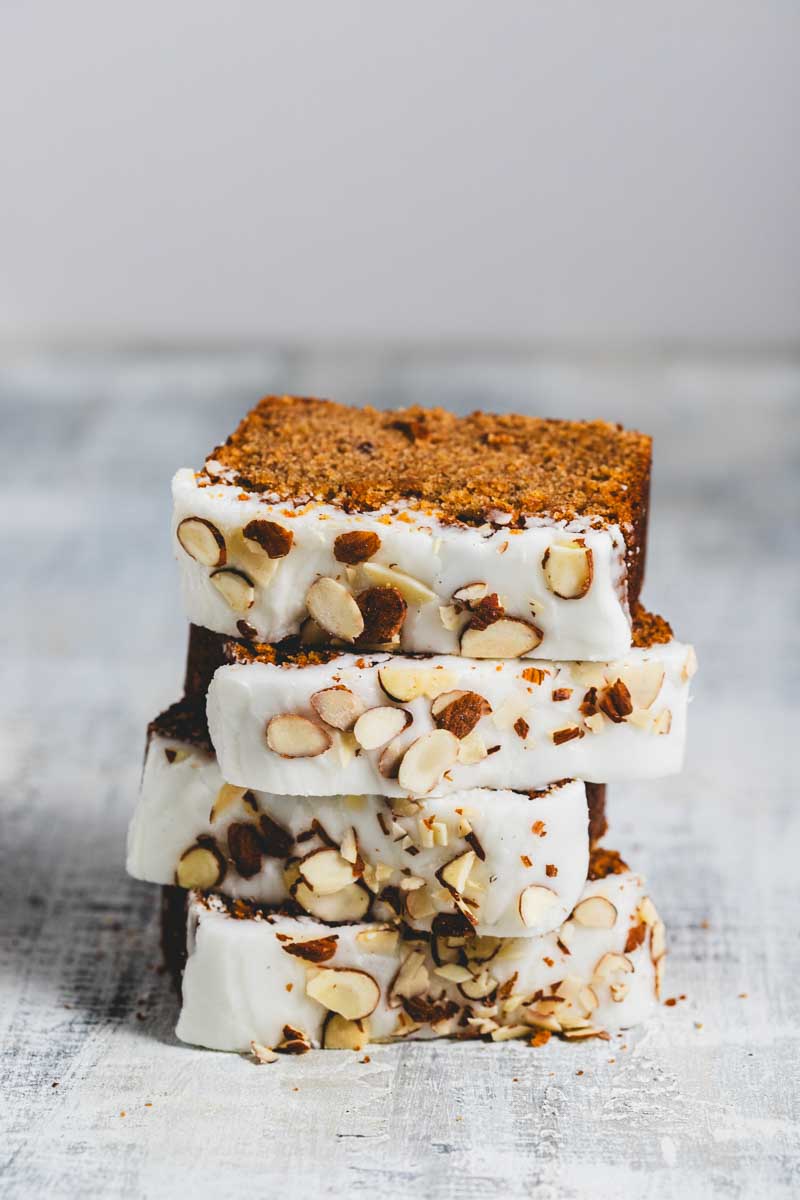 stacked slices of lemon almond loaf with frosting and sliced almonds on top