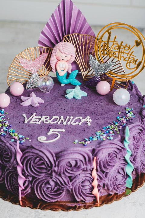 Purple birthday cake with decorative elements and 'Happy Birthday' topper