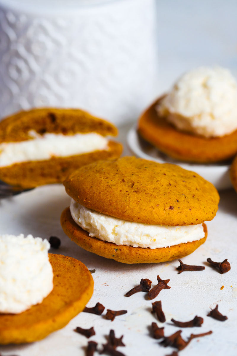 Pumpkin whoopies with cream filling on a white surface with star anise.