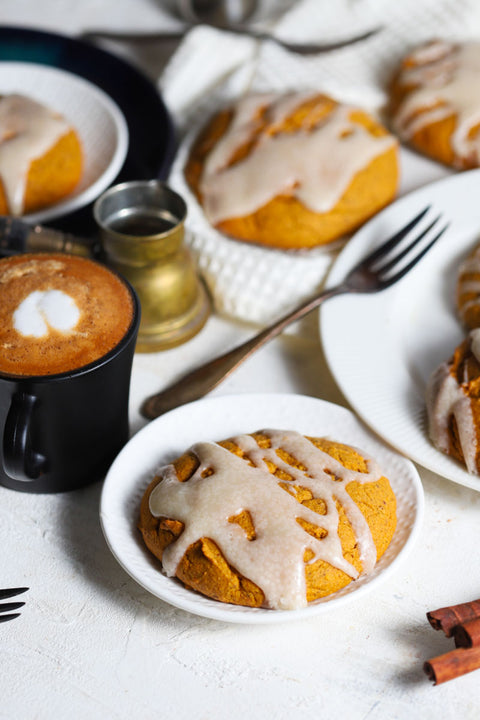 Pumpkin scones with cheesecake icing on white and black plates with cinnamon and coffee