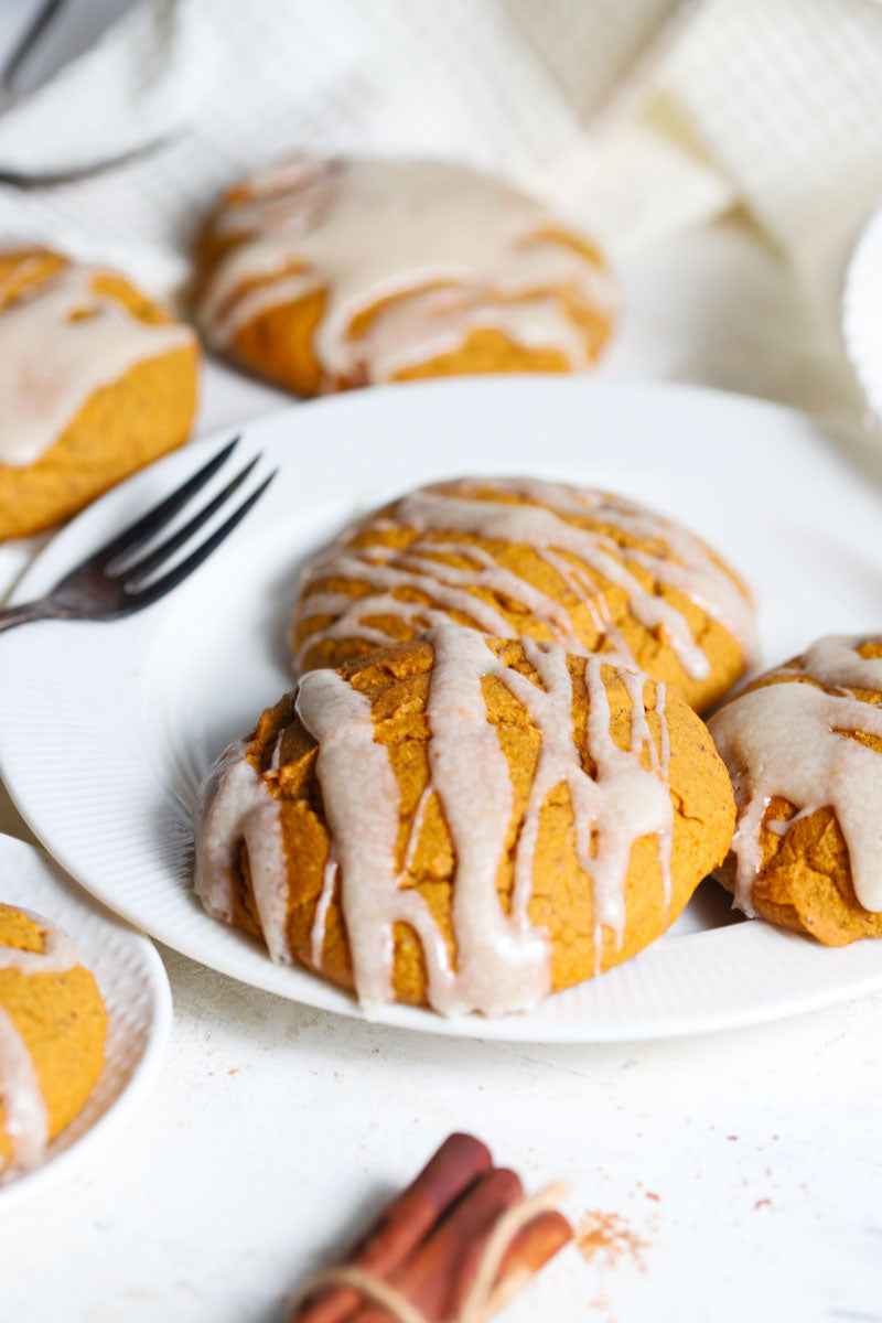 Pumpkin scones with cheesecake icing on a white plate with cinnamon sticks