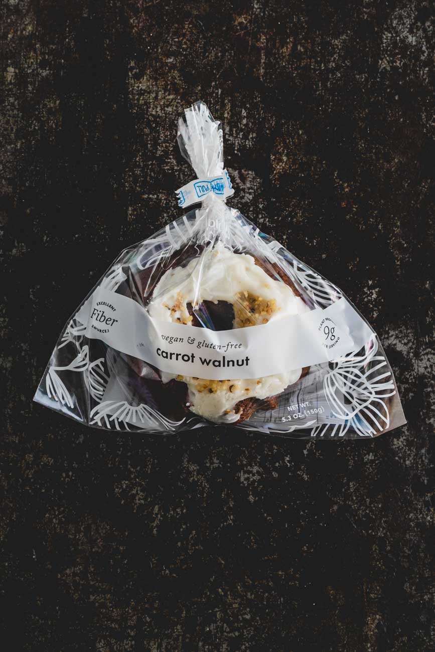 Top down view of a mini carrot walnut bundt cake with icing and crushed walnuts on top wrapped in a plastic bag