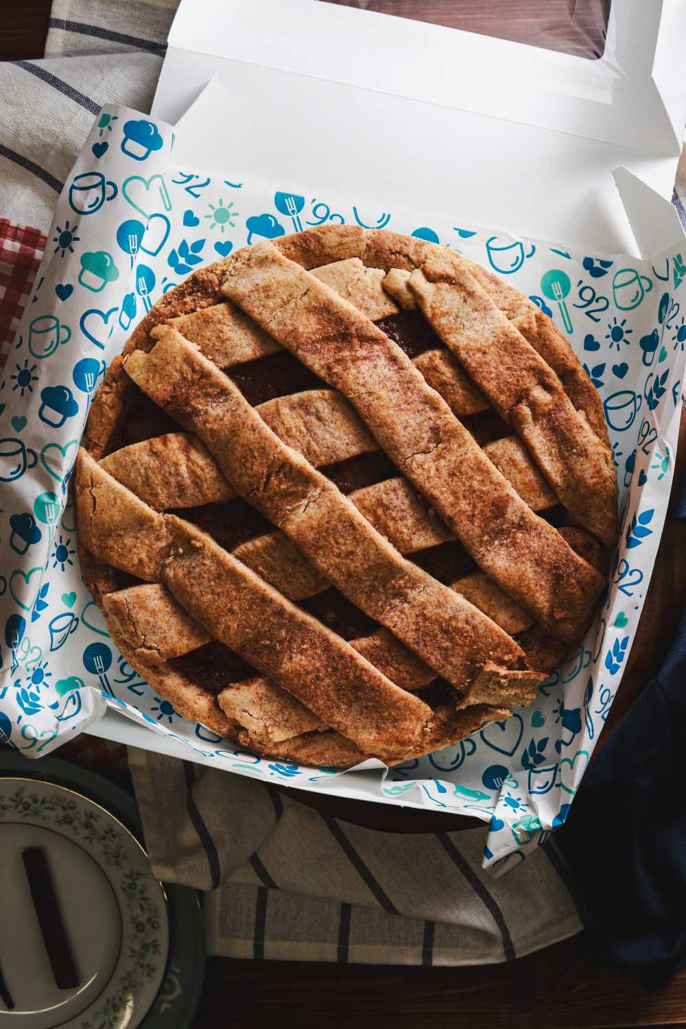 Whole apple pie with a lattice crust in a white box with a decorative liner, ready for gifting.