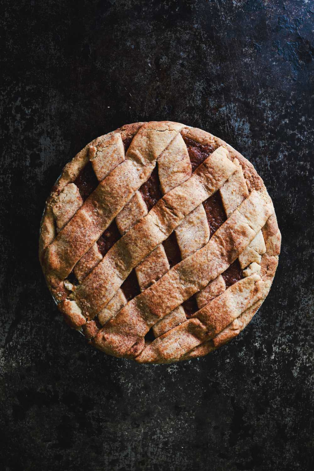 Whole apple pie with a lattice crust, displayed on a dark rustic surface.