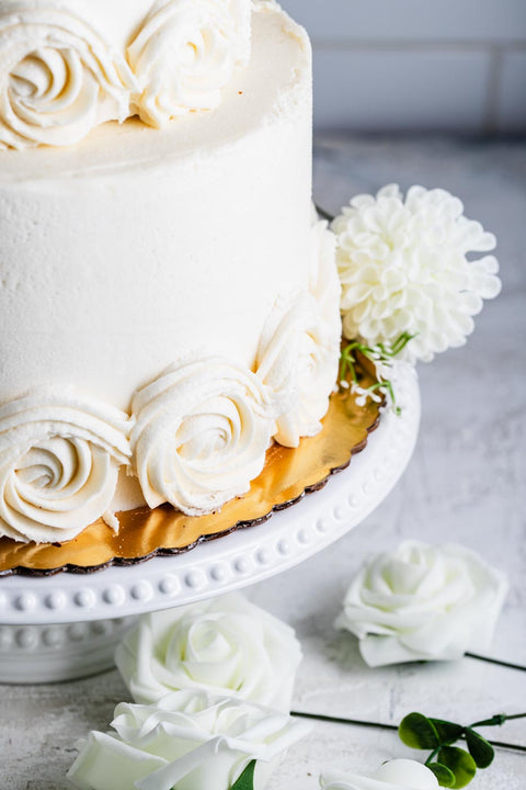A close up of a tiered wedding cake on a white cake stand showing detail of white frosting flowers and decorative white flowers