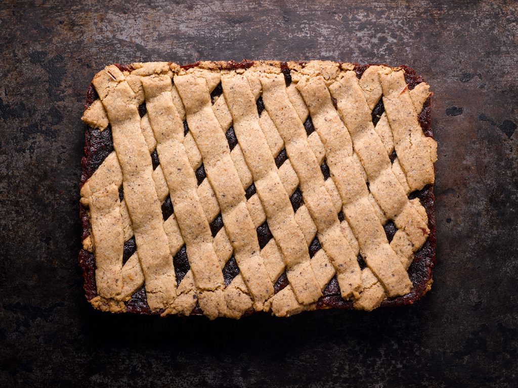 A full raspberry hazelnut bar with a crisscrossed lattice top, placed on a dark background.
