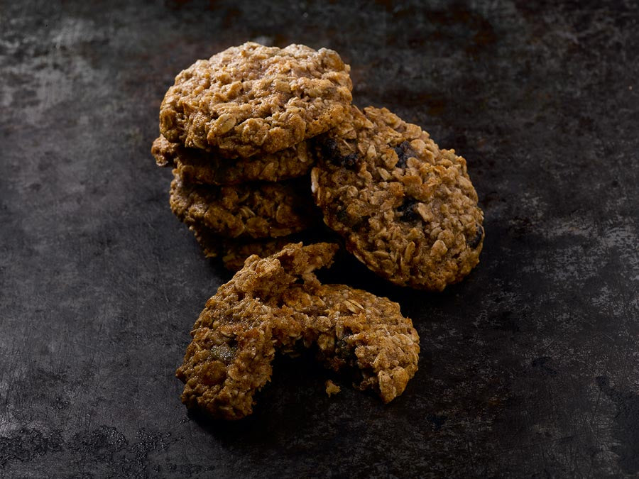 Stack of energy cookies with one cookie broken in half, showing a chewy texture with oats and raisins.