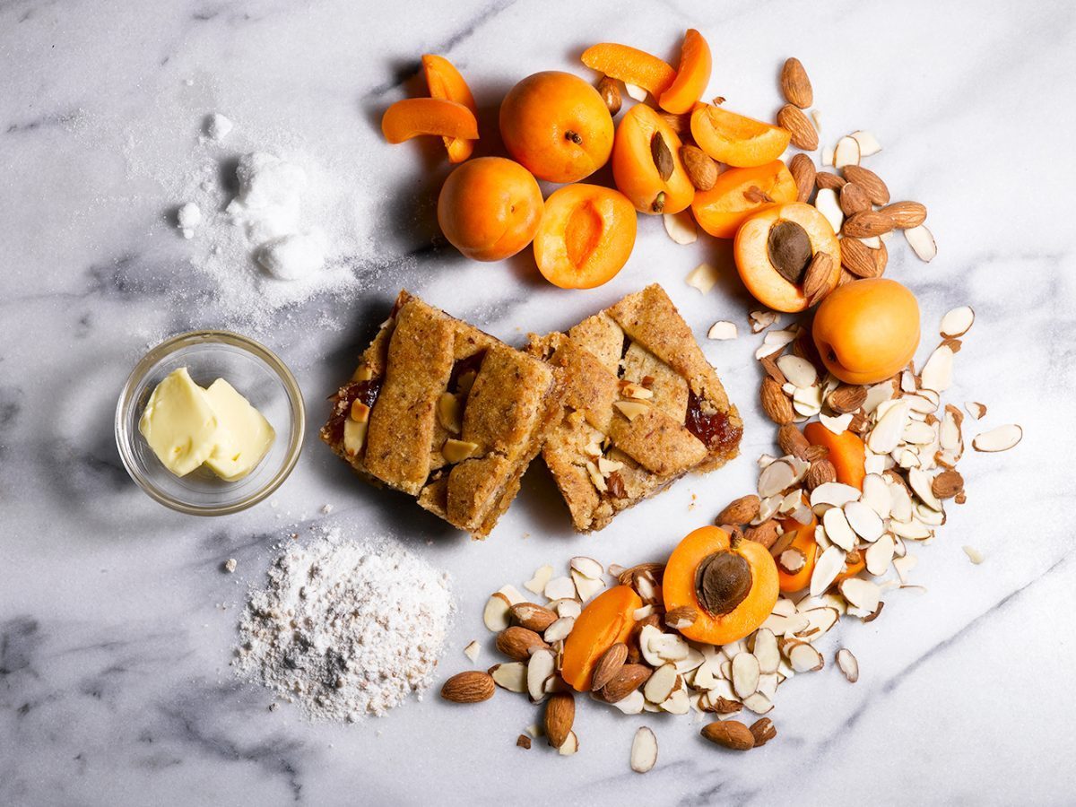 Apricot almond bars on a marble background surrounded by apricots, and sliced almonds.