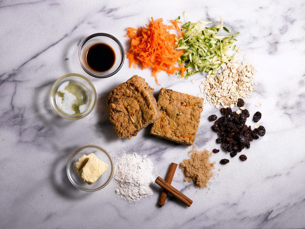 Ingredients for grassroot bar laid out on a marble surface, including shredded carrots, zucchini, oats, raisins, and cinnamon.