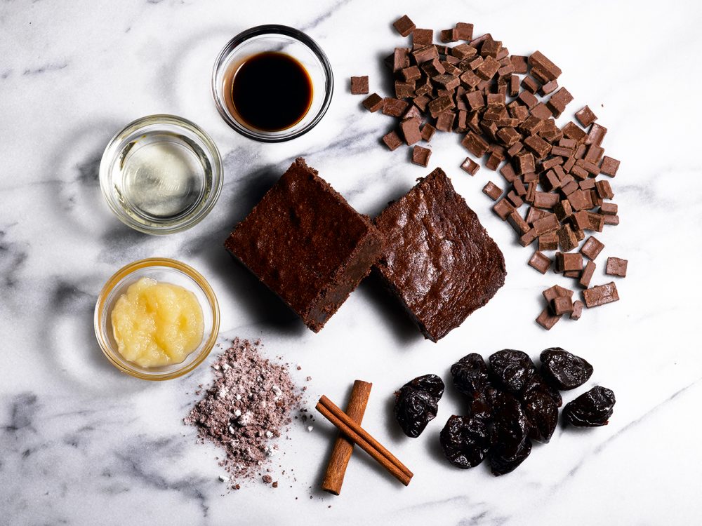 Chocolate chunk brownie with ingredients: applesauce, cinnamon sticks, prunes, chocolate chunks, vanilla extract, oil, cocoa powder.