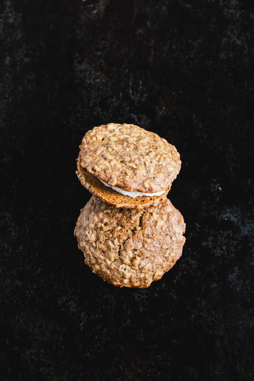 Top view of two oatmeal cream whoopie pies on a dark background, emphasizing the oatmeal texture and creamy filling.