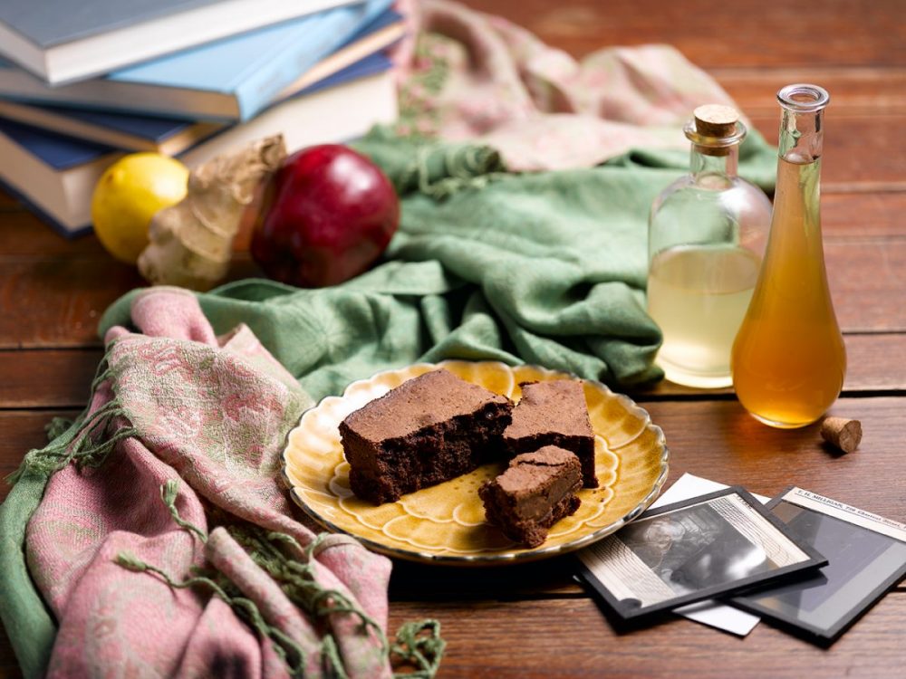 Delicious chocolate chunk brownie on a decorative plate, surrounded by fresh ingredients and bottles of homemade extracts.