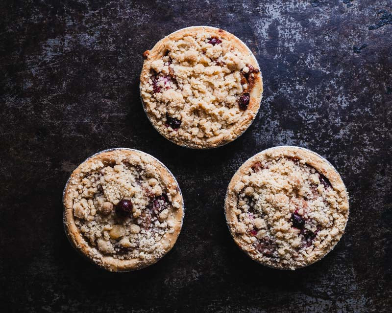 Three mini cranberry apple pies with crumb toppings arranged in a triangle on a rustic background.