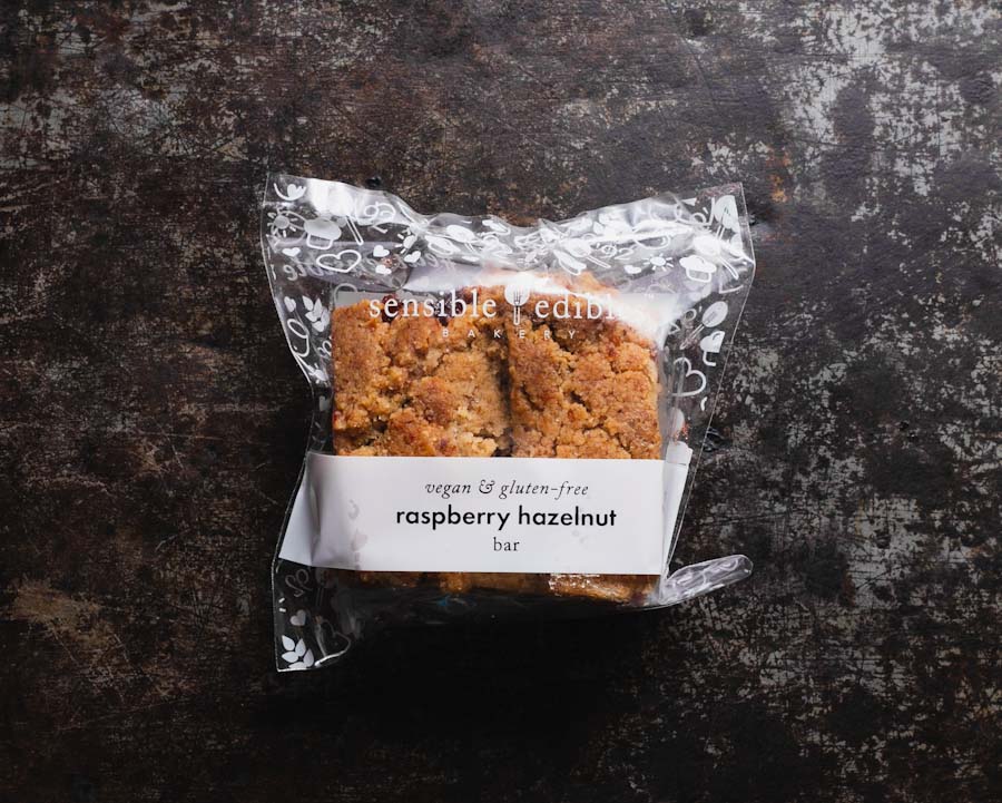 A packaged raspberry hazelnut bar from Sensible Edibles Bakery, labeled "vegan & gluten-free," in a clear packaging.
