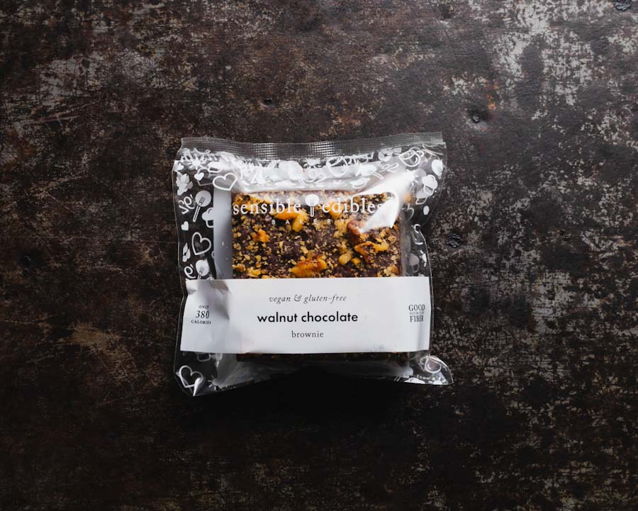 Packaged walnut brownie labeled 'Sensible Edibles Walnut Chocolate Brownie' in a clear packaging, against a dark background.