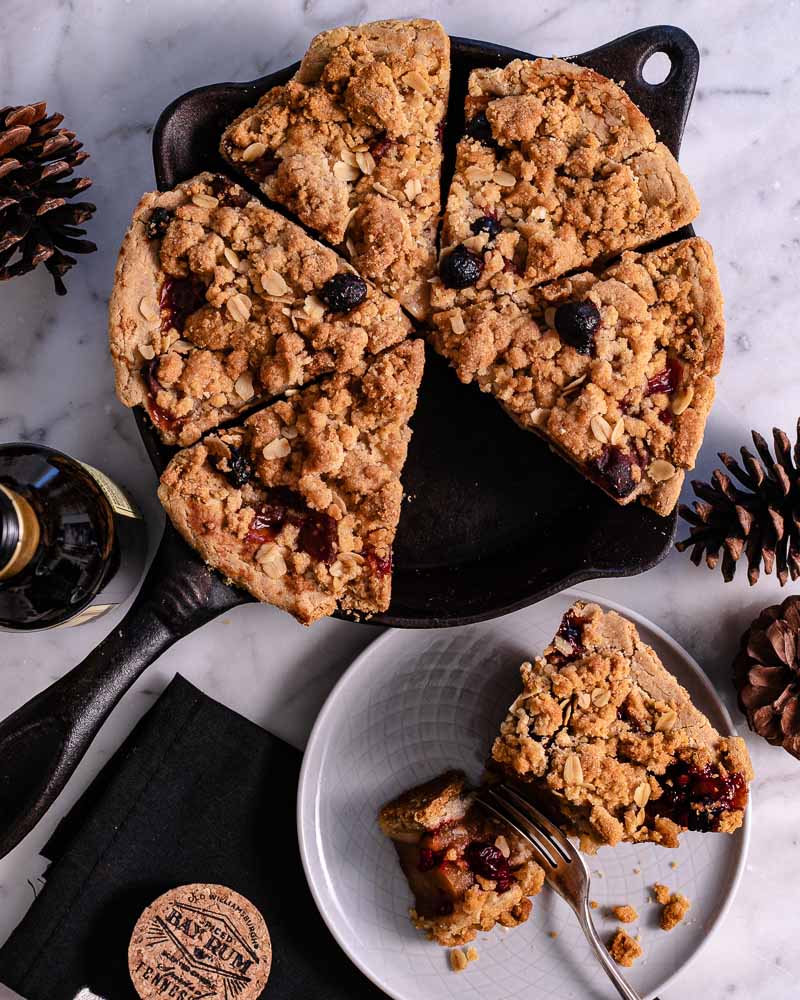Sliced cranberry apple pie with a crumb topping in a cast iron skillet, served with a slice on a white plate."